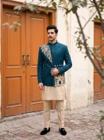 Royal teal blue Jacquard prince coat featuring intricate handmade golden embroidery, floral motifs, and a Mandarin collar, styled with a cream kurta pajama for a luxurious traditional wedding look.